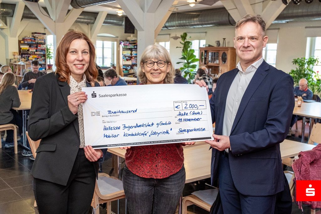 drei Menschen halten einen großen Scheck in den Händen 