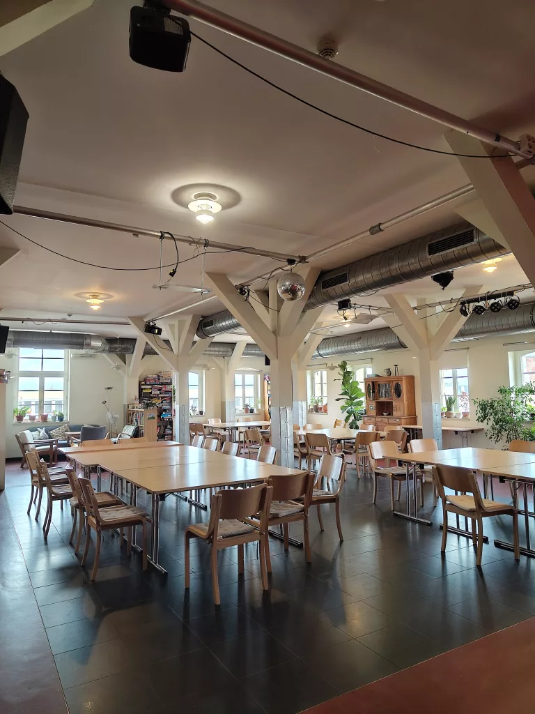 Tische und Stühle aus Holz in einem großen Saal mit Fenstern im Hintergrund