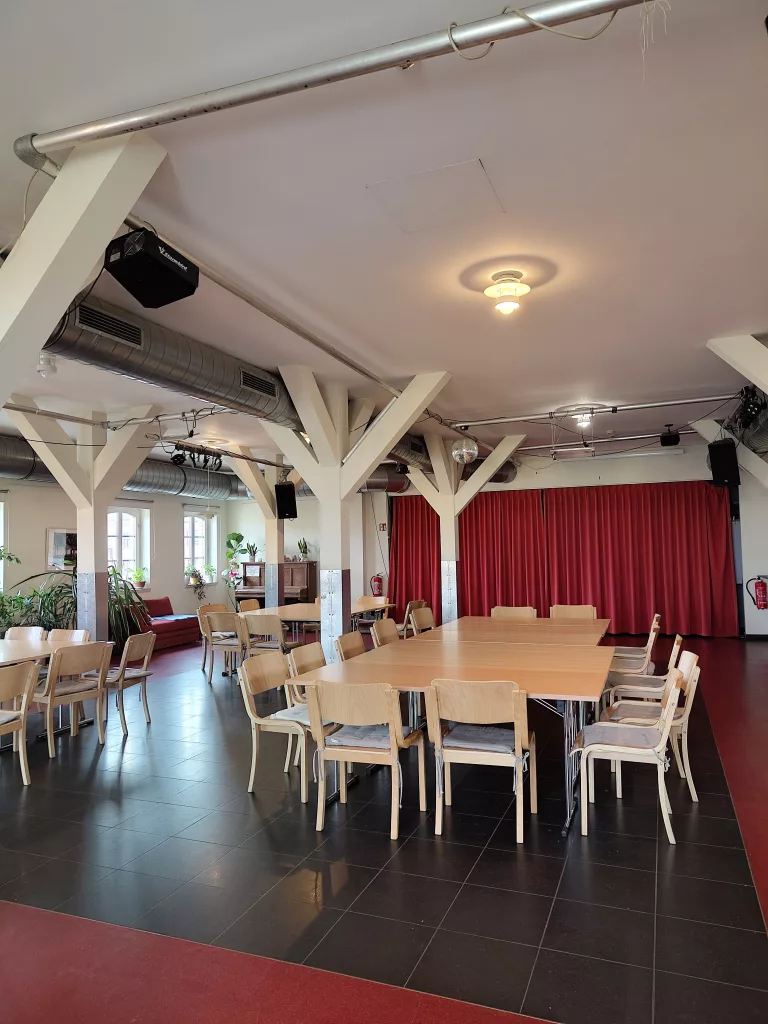 Tische und Stühle aus Holz in einem großen Saal mit einem roten Vorhang im Hintergrund