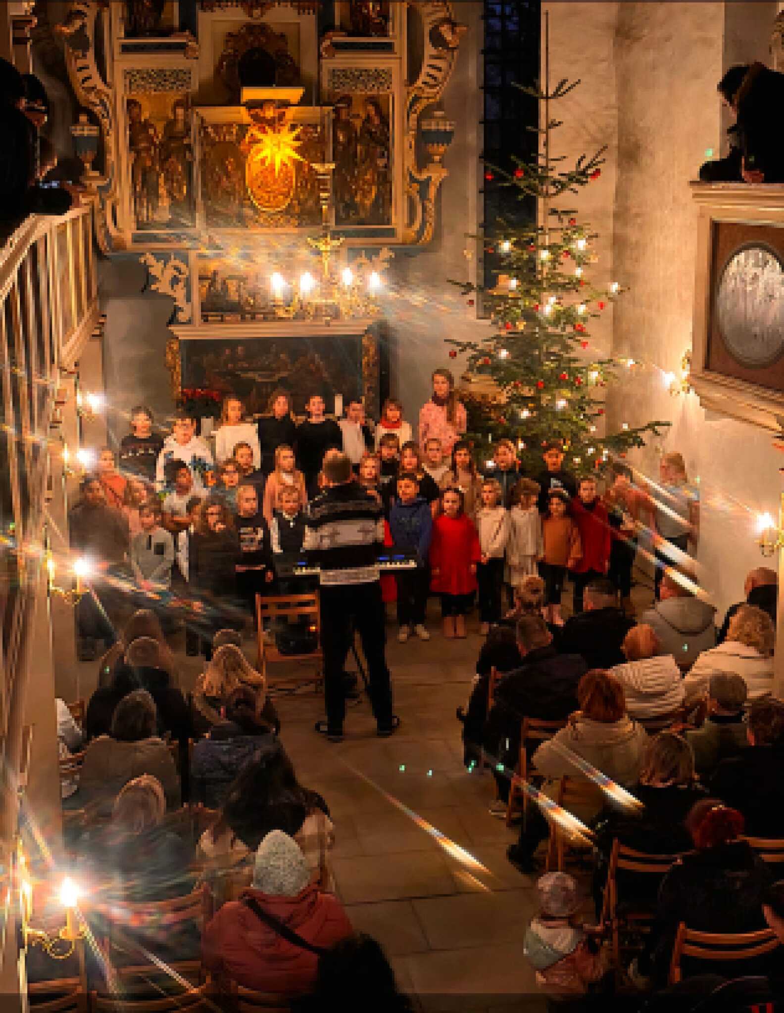 Kinder singen neben einer geschmückten Tanne in einer beleuchteten Kirche
